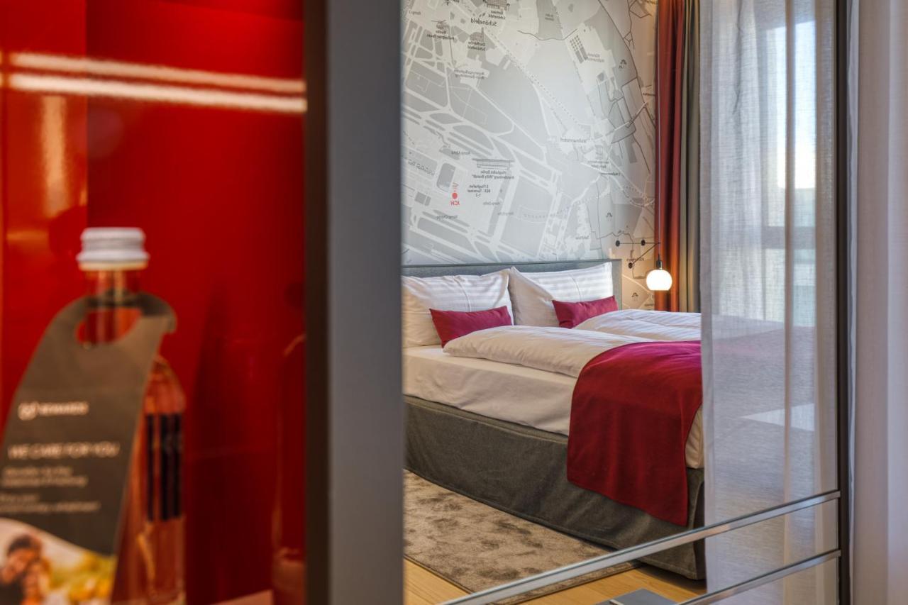 Intercityhotel Berlin Airport Ber Terminal 1 & 2 舍讷费尔德 外观 照片 The photo shows a modern hotel room that features a comfortable bed with white linens and a red accent blanket. Behind the bed is a stylish wall displaying a map design. The room has large windows dressed with light-colored curtains, allowing natural